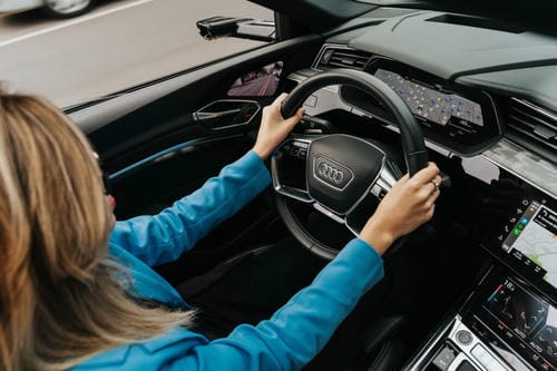 A woman behind the wheel of an Audi, driving the car with hands on the steering wheel, surrounded by modern digital displays.