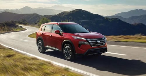 A red Nissan SUV driving on a winding mountain road.