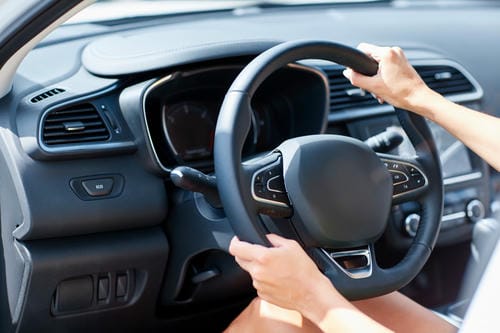 A close-up of a driver's hands on the steering wheel, showing a modern car's interior.