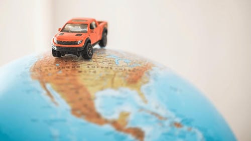 A small orange toy pickup truck sitting atop a globe of North America, symbolizing global travel.