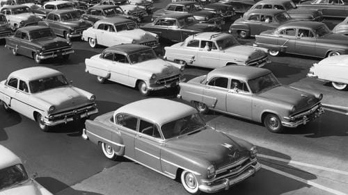 A black-and-white photo of heavy traffic filled with vintage cars from the 1950s.
