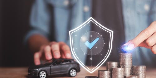 A shield with a checkmark overlaying a toy car and stacks of coins, symbolizing financial security for vehicle ownership.