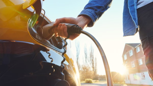 A person plugging a charging cable into an electric vehicle outdoors.