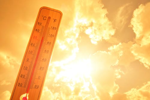 A thermometer indicating high temperatures under a bright, sunny sky.