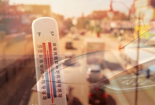 A thermometer showing high temperatures against a city traffic background.