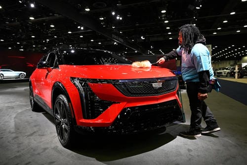 A person cleaning a bright red Cadillac vehicle at an auto show.