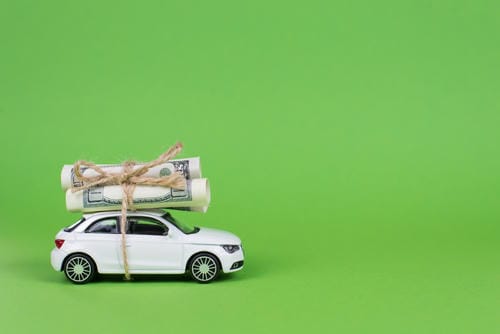 A white toy car carrying rolls of cash tied with string, symbolizing car-related expenses.
