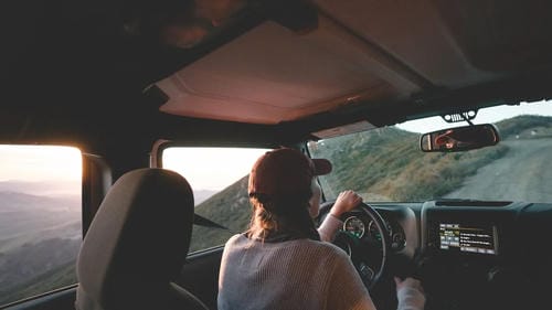 A person driving a Jeep off-road through a mountainous landscape at sunset.
