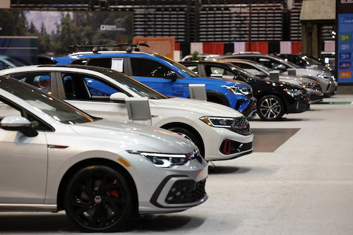 A row of new Volkswagen cars, including a GTI and Arteon, on display at an indoor auto show.
